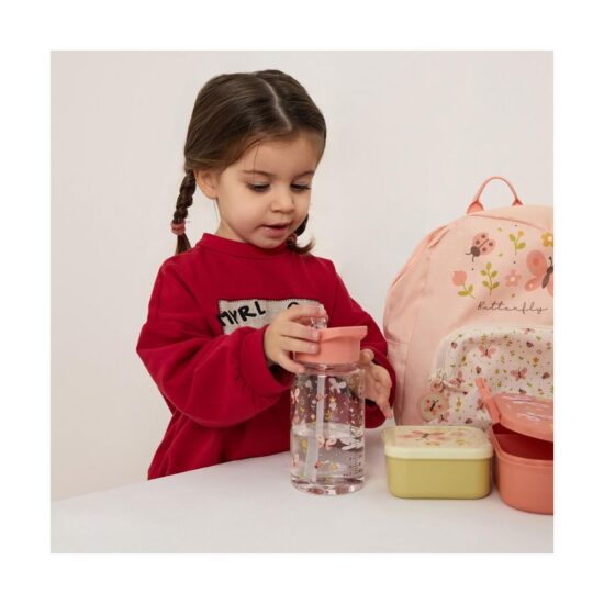 Young girl with braided pigtails in a red sweatshirt places a pink-lidded water bottle on a table beside pastel lunch boxes and a pink butterfly backpack.
